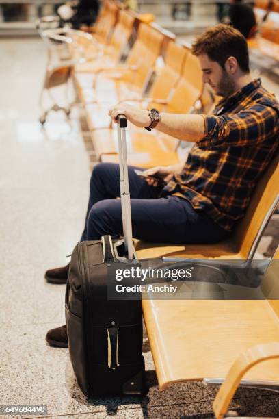 homme adulte assis dans la salle d’embarquement avant son vol - salle dembarquement photos et images de collection