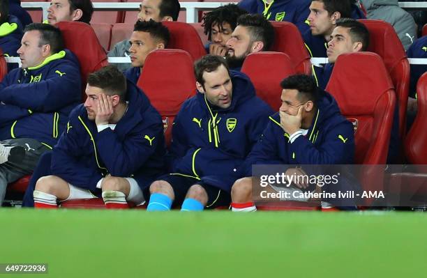 Alexis Sanchez appears to smirk as he, Aaron Ramsey and Petr Cech of Arsenal watch from the bench during the UEFA Champions League Round of 16 second...