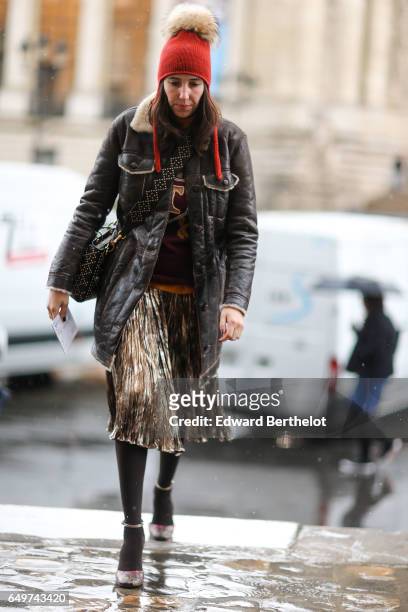 Guest wears an orange beanie hat with a pompom, an aviator jacket, a pleated skirt, outside the Elie Saab show, during Paris Fashion Week Womenswear...