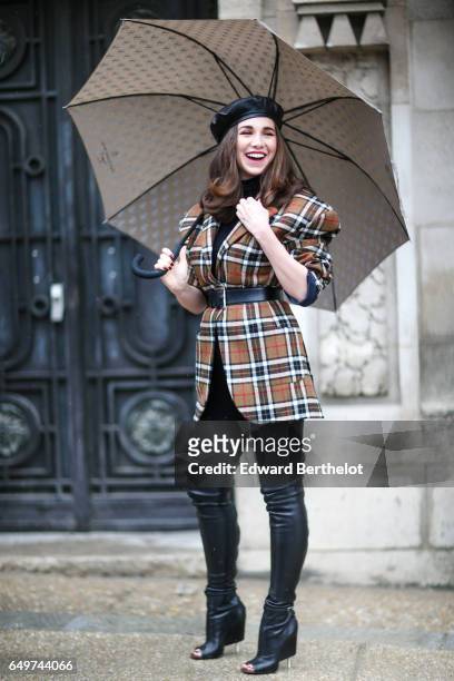 Guest wears a checked jacket, and black thigh high leather boots, and an umbrella, outside the Elie Saab show, during Paris Fashion Week Womenswear...