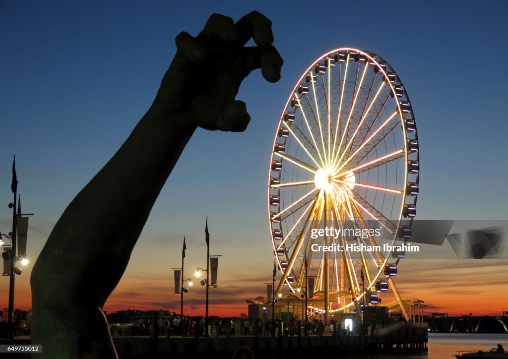 National Harbor and The Capital Wheel illuminated at Dusk featuring The Awakening statue, Maryland, USA.