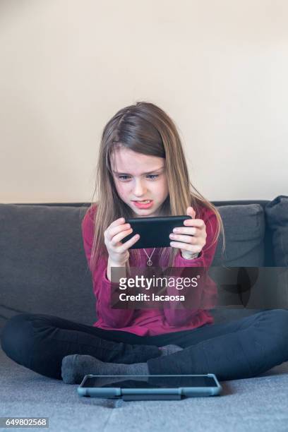 angry girl playing on a smartphone - lacaosa stock-fotos und bilder