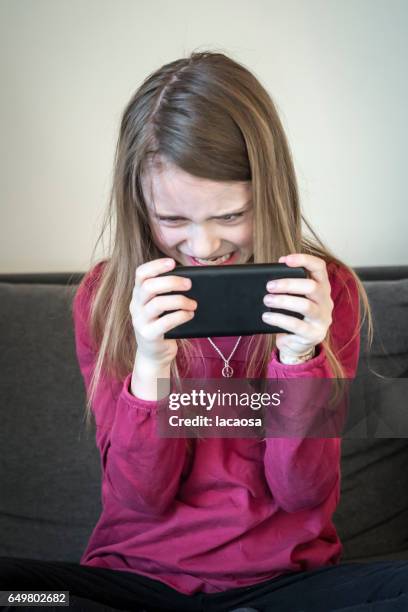 angry girl playing on a smartphone - lacaosa stock-fotos und bilder