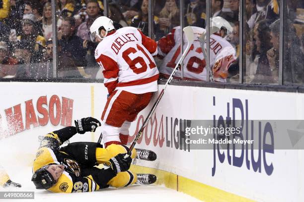 Tim Schaller of the Boston Bruins slides into the boards past Xavier Ouellet of the Detroit Red Wings during the first period at TD Garden on March...