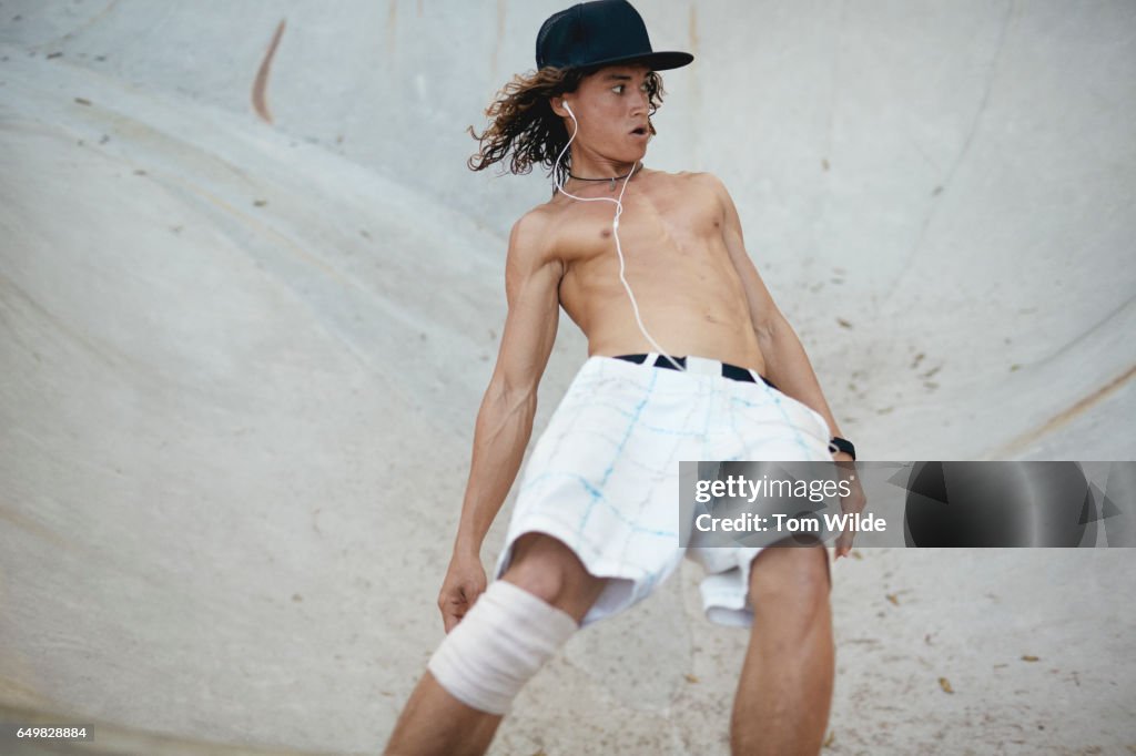 Barefoot young male skateboarder skates in a a concrete bowl