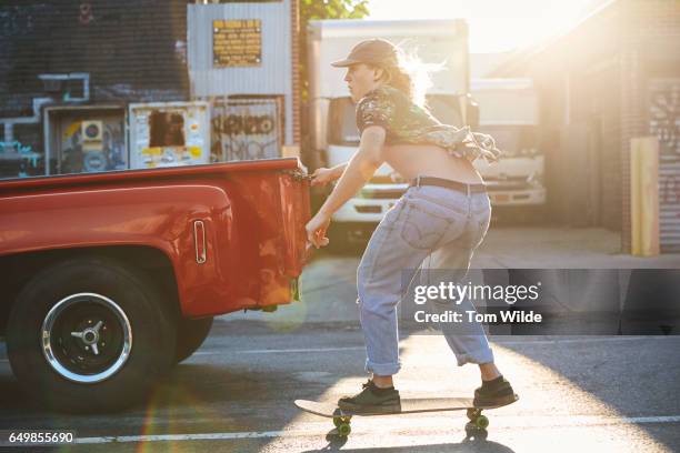 male skateboarder skitching a red truck as it drives through the emory streets of brooklyn, new york - active in new york stock pictures, royalty-free photos & images