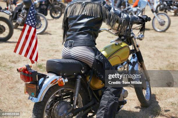 rear view of a leather clad, female biker as she rides her yellow motorbike - motorbike flag stock pictures, royalty-free photos & images