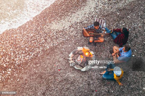 young friends enjoying music near campfire - bonfire beach stock pictures, royalty-free photos & images