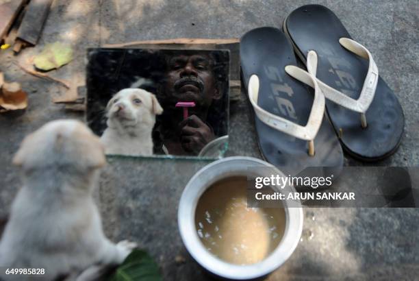 Homeless Indian man and his puppy are reflected in a mirror as he shaves himself on a street in Chennai on March 9, 2017.