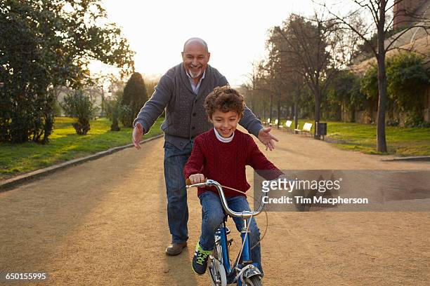 grandfather teaching grandson to ride bicycle in park - fahrrad fahren großeltern mit kind stock-fotos und bilder
