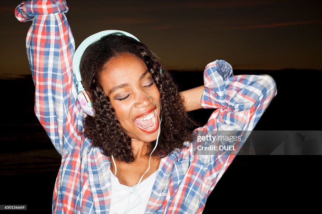 Young woman wearing headphones arm raised, eyes closed open mouthed smiling