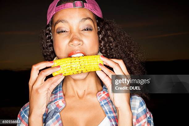 young woman biting corn on the cob looking at camera - corn cob photos et images de collection