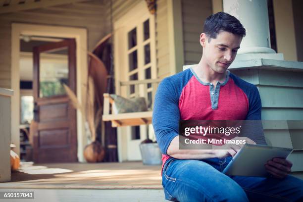 a man sitting relaxing in a quiet corner of a porch, using a digital tablet.  - hollywoodschaukel stock-fotos und bilder