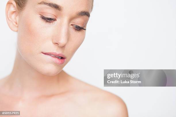 bare shouldered woman looking down biting lip - biting lip stock pictures, royalty-free photos & images