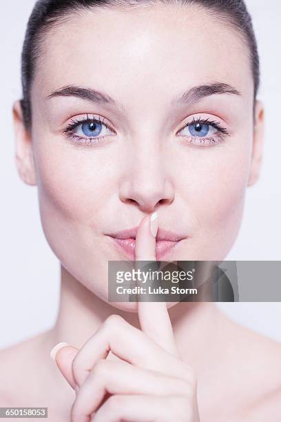 head and shoulder shot of beautiful young woman with finger on lips - natural portrait studio shot white background stock-fotos und bilder