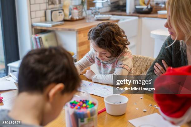 three children and an adult woman at a table, drawing and writing cards and letters to santa.  - christmas colouring stock pictures, royalty-free photos & images