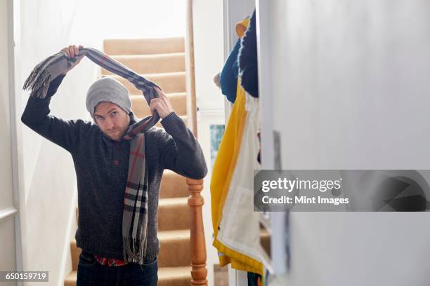 a man in a winter coat, hat and scarf arriving home, taking his scarf off.  - arriving home stock pictures, royalty-free photos & images