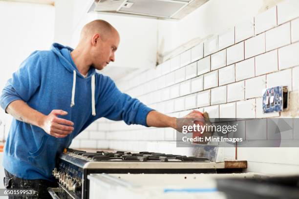 a man working in a new kitchen, a tiler applying tiles to the wall behind the cooker.  - mörtel stock-fotos und bilder