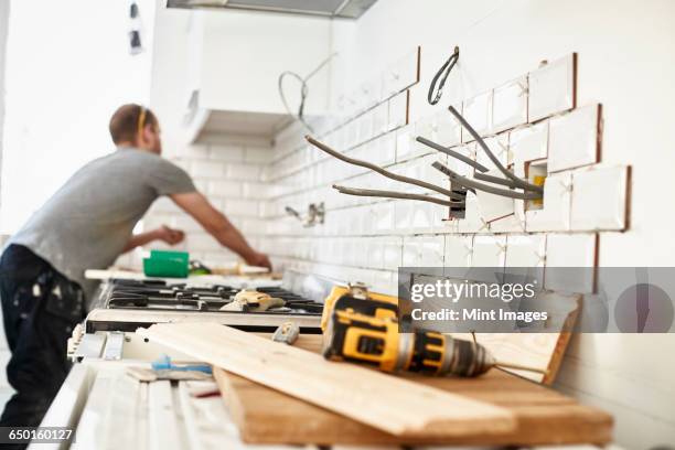 a man working in a new kitchen, a tiler applying tiles to the wall behind the cooker.  - home improvement stock pictures, royalty-free photos & images