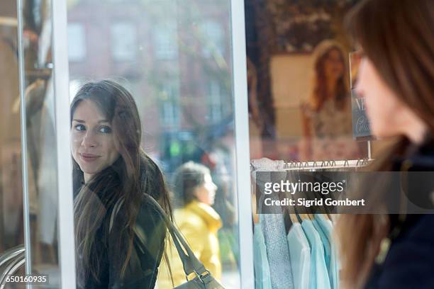 woman carrying handbag looking into shop mirror smiling - sigrid gombert stock-fotos und bilder