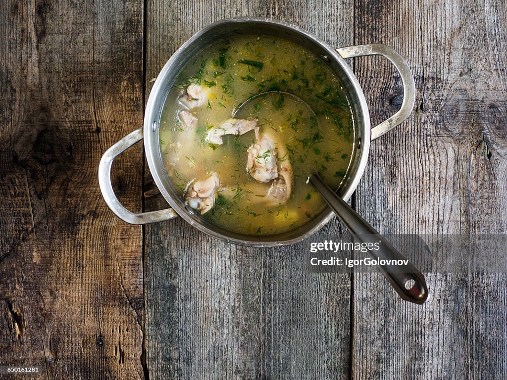 Saucepan of chicken soup on wooden table