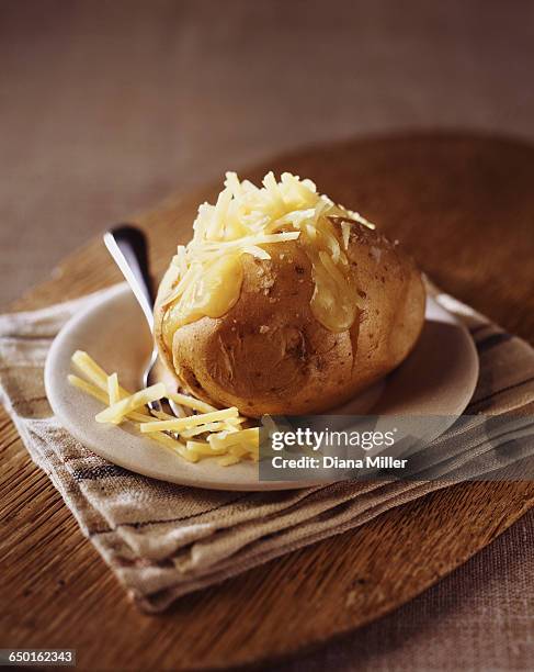 baked potato with grated cheddar cheese on wooden cutting board - baked potato foto e immagini stock