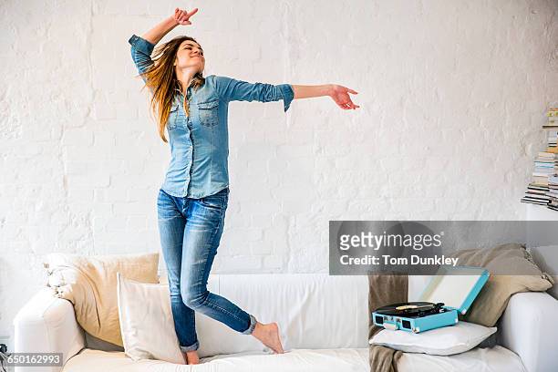 young woman standing on sofa dancing to vintage record player - double denim photos et images de collection
