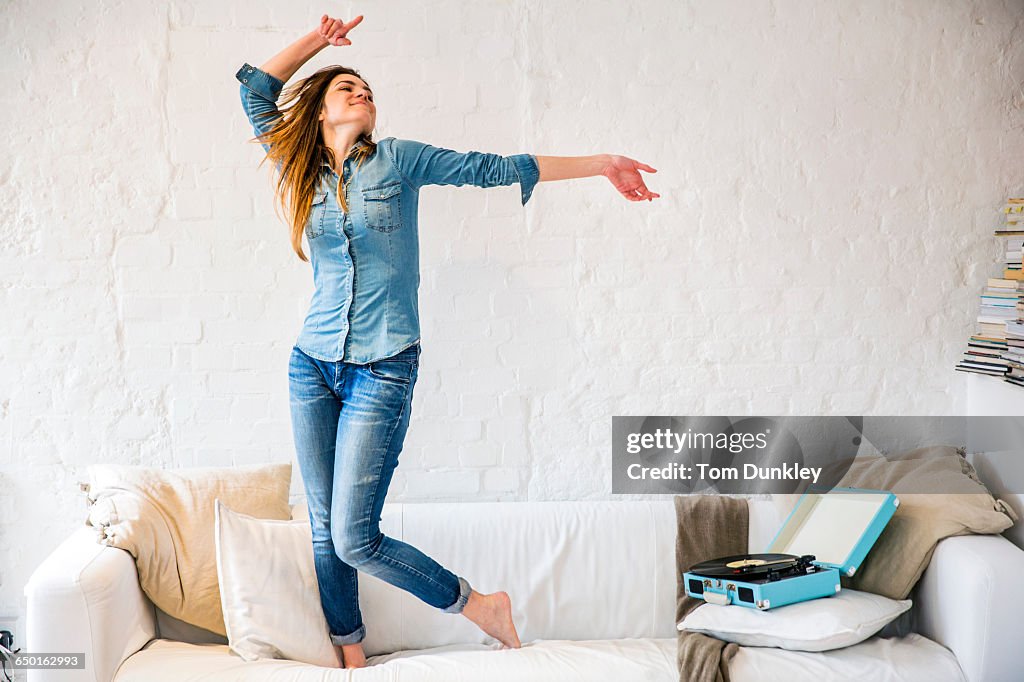 Young woman standing on sofa dancing to vintage record player