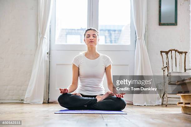 young woman practicing yoga lotus position in apartment - salle yoga photos et images de collection