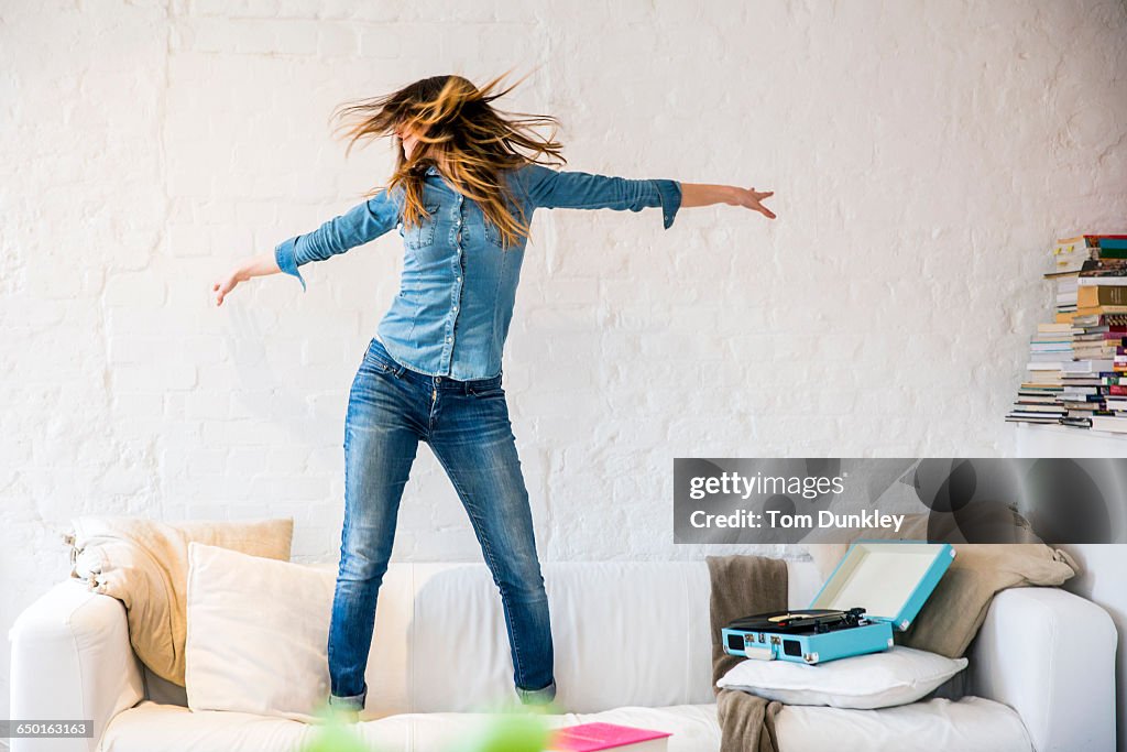 Young woman standing on sofa dancing and shaking her hair