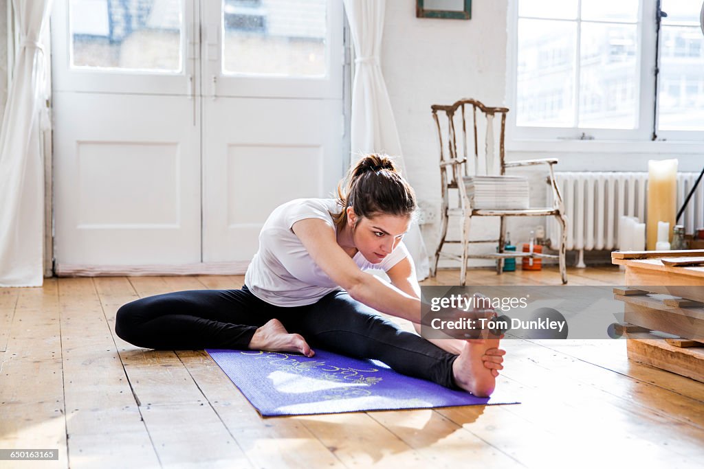 Young woman practicing yoga, touching toes in apartment