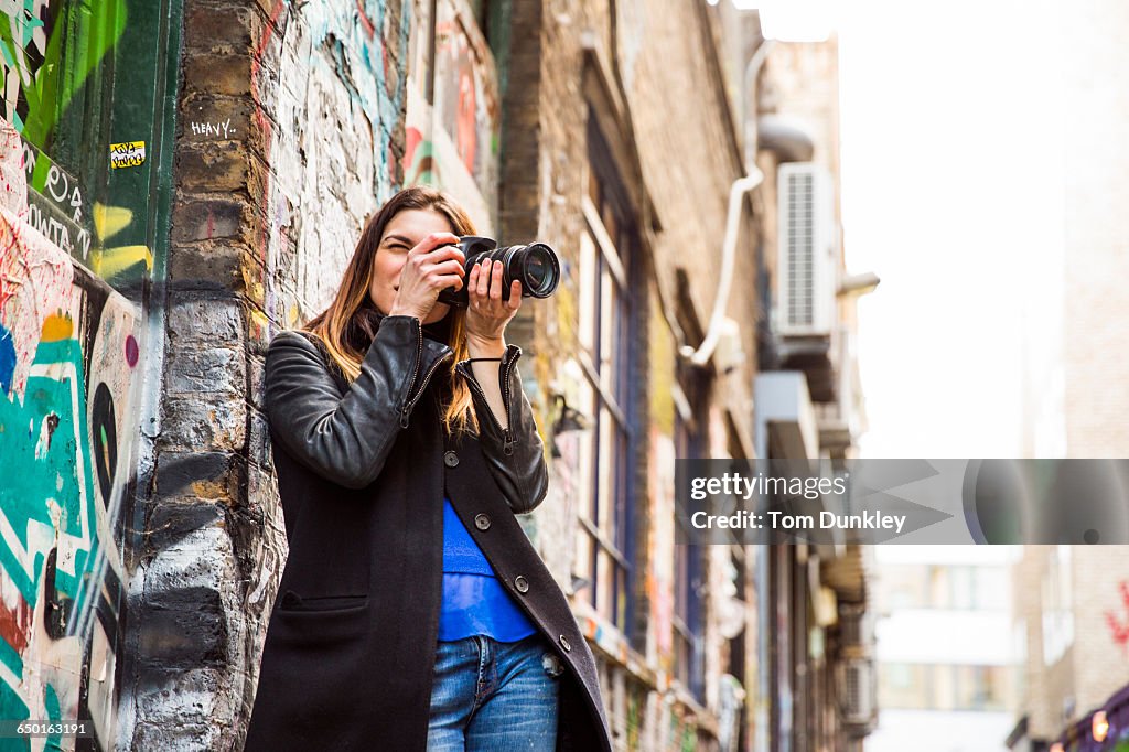 Young woman photographing in graffiti alley using DSLR