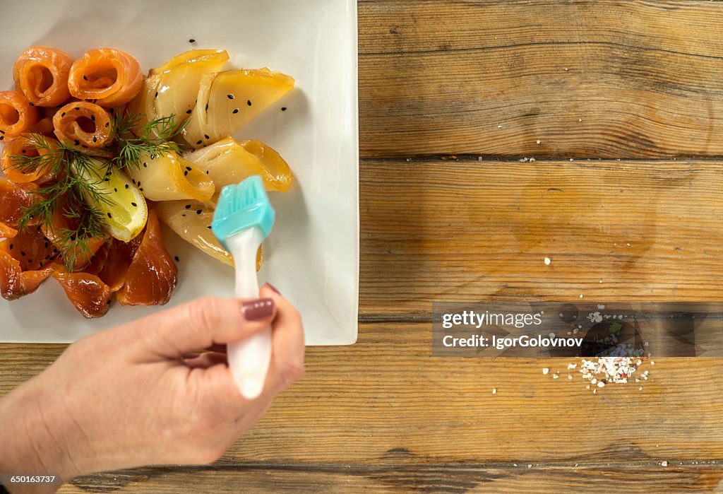 Woman's hand glazing slices of salmon and starry sturgeon fish, Ukraine