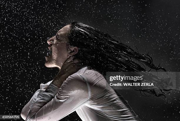side view of woman wearing white shirt drenched in rain throwing back hair - nasses haar stock-fotos und bilder