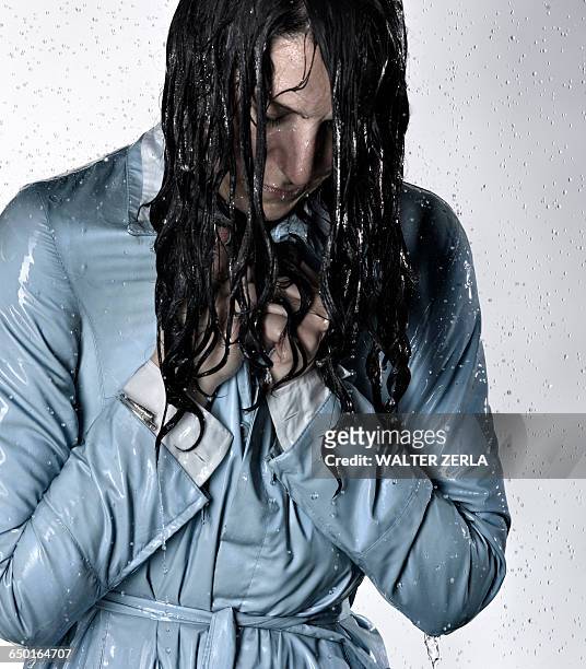 woman wearing raincoat drenched in water looking down - doorweekt stockfoto's en -beelden