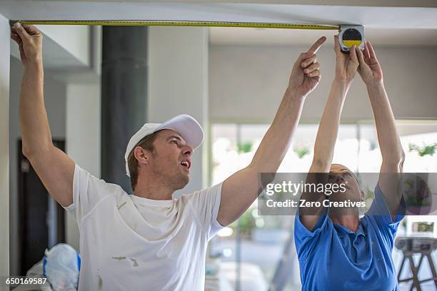 couple, arms raised, using tape measure to measure ceiling - woman measuring tape stock pictures, royalty-free photos & images