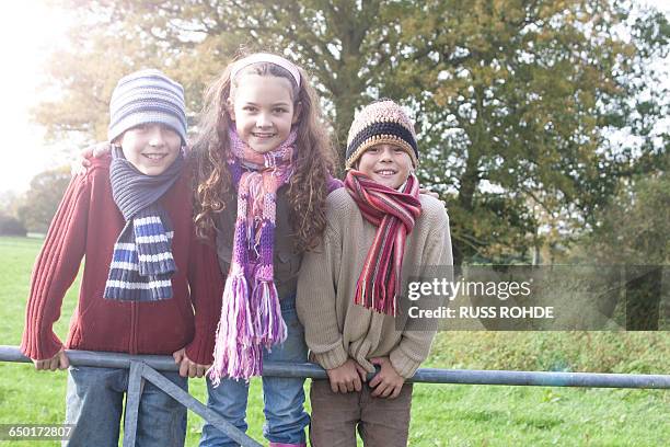 portrait of three children leaning on fence, smiling - 子供のみ ストックフォトと画像