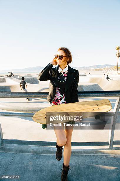 young woman standing by railings, near skate park, holding skateboard - venice stock-fotos und bilder