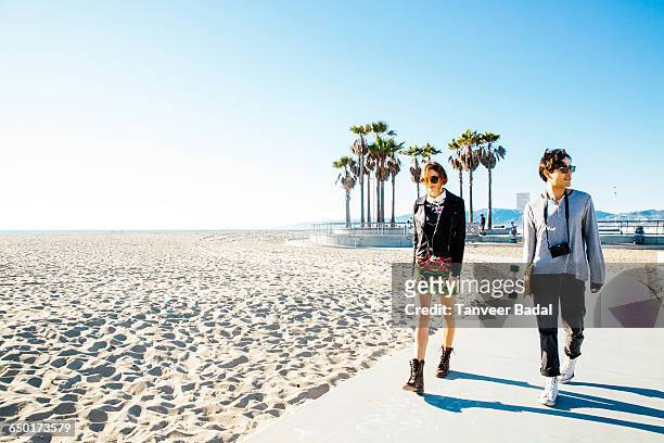 young couple walking along beach walkway - a la moda stock pictures, royalty-free photos & images