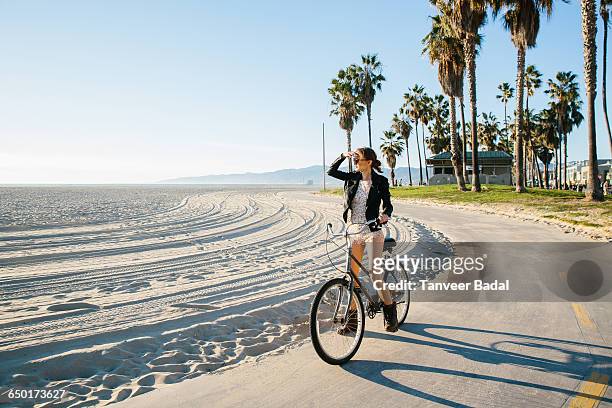 young woman cycling at beach looking out to sea, venice beach, california, usa - los angeles photos et images de collection