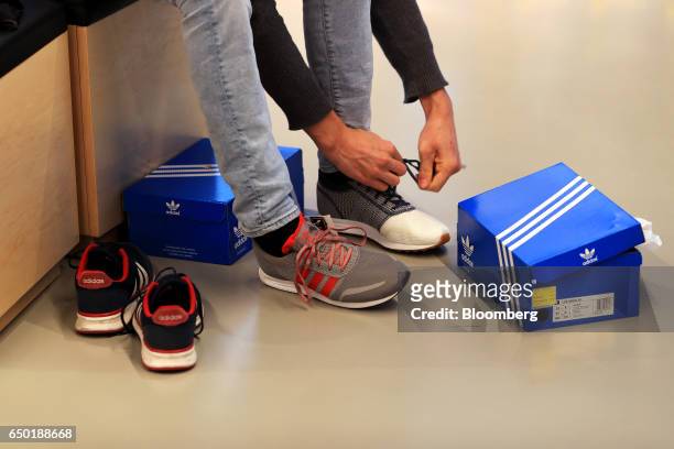 Customer tries on two styles of sneaker at an Adidas AG retail store in Herzogenaurach, Germany, on Wednesday, March 8, 2017. Adidas' new chief...