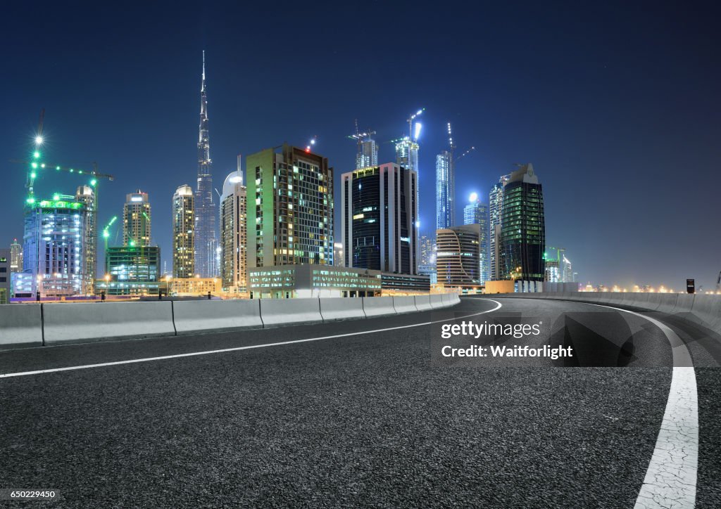 Urban asphalt road with dubai skyline background at night