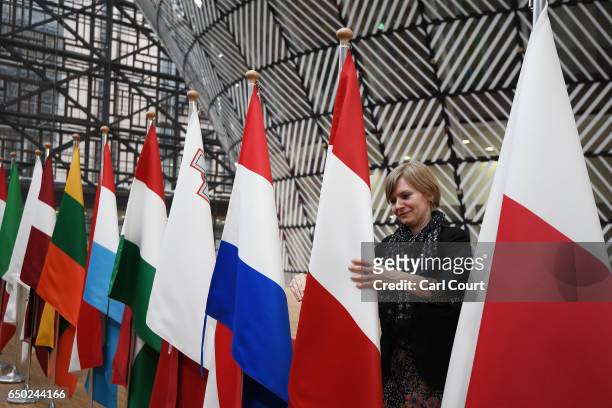 Woman adjusts a flag in the arrival area of the Europa building at the Council of the European Union on the first day of an EU summit, on March 9,...