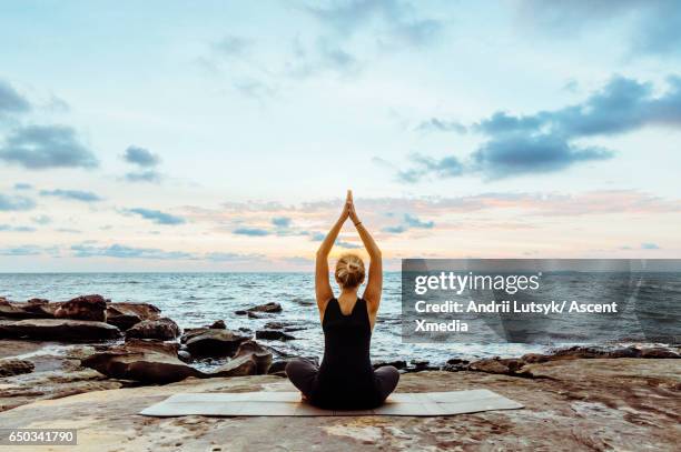 young woman performs yoga moves on bluff above sea - meditieren stock-fotos und bilder