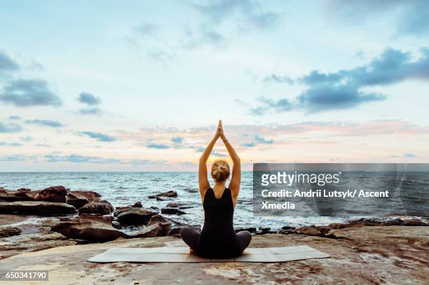 young woman performs yoga moves on bluff above sea - yoga outdoor foto e immagini stock