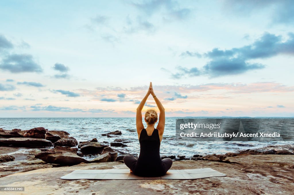 Young woman performs yoga moves on bluff above sea