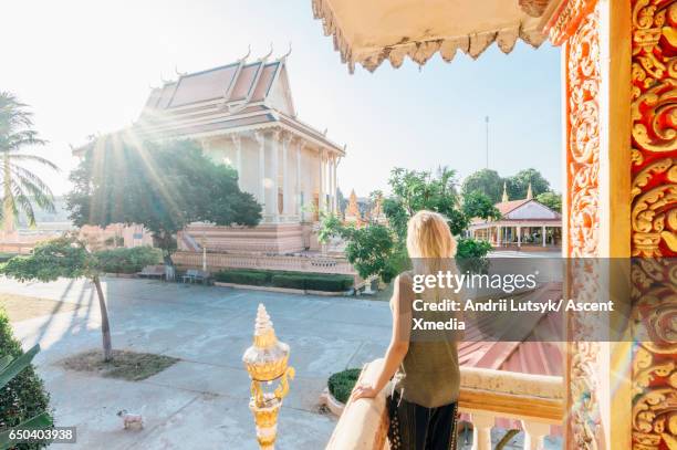 young woman looks off from balcony of pagoda, sunrise - kambodschanische kultur stock-fotos und bilder