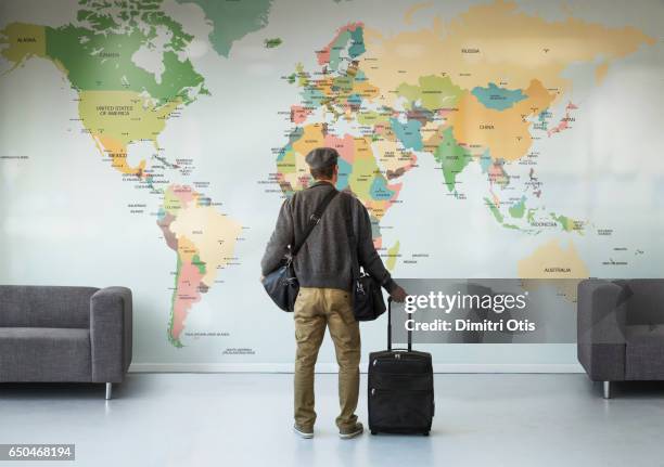 man with luggage looking at large wall map - navigationsinstrument stock-fotos und bilder
