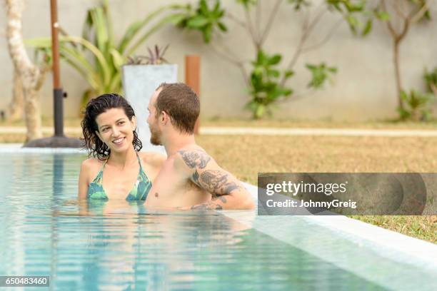 mid adult woman talking to man with tattoos in pool - cool couple in apartment stock pictures, royalty-free photos & images