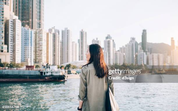 pretty young girl enjoying the city view by the sea on a fresh morning - commercial buildings hong kong morning stock pictures, royalty-free photos & images